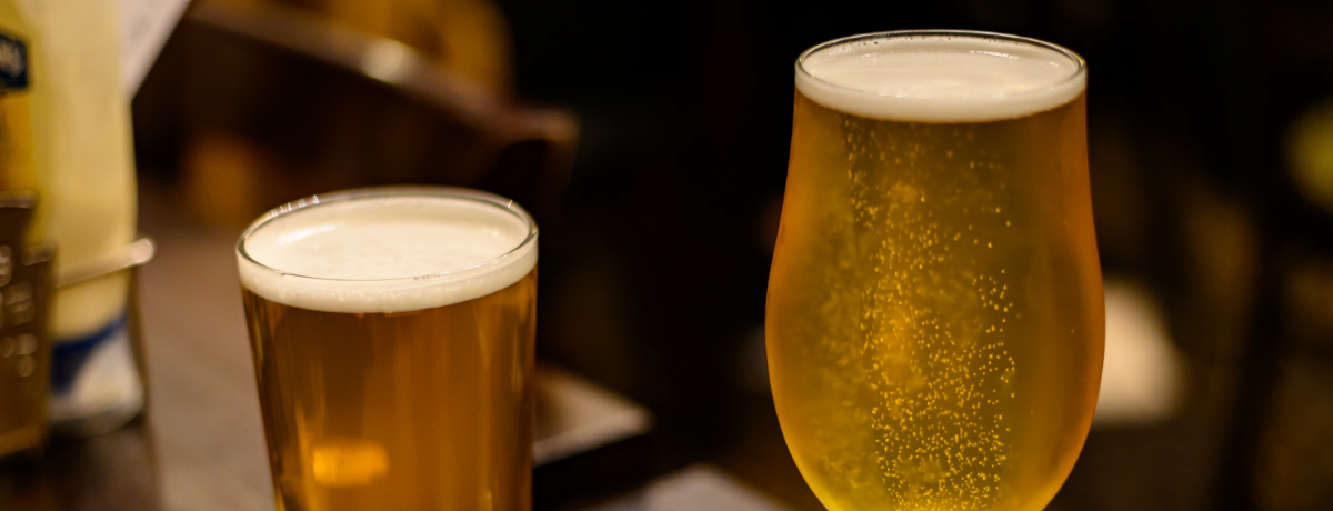 Zwei Gläser mit hellem Ale und Pale Ale auf einem Holztisch, Hintergrund unscharf, Bar-Atmosphäre