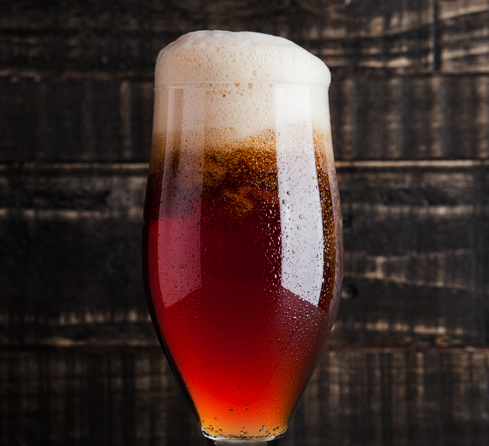 Rotbraunes Bier mit dichter Schaumkrone in beschlagenem Glas vor dunkler Holzoberfläche, senkrecht inszeniert